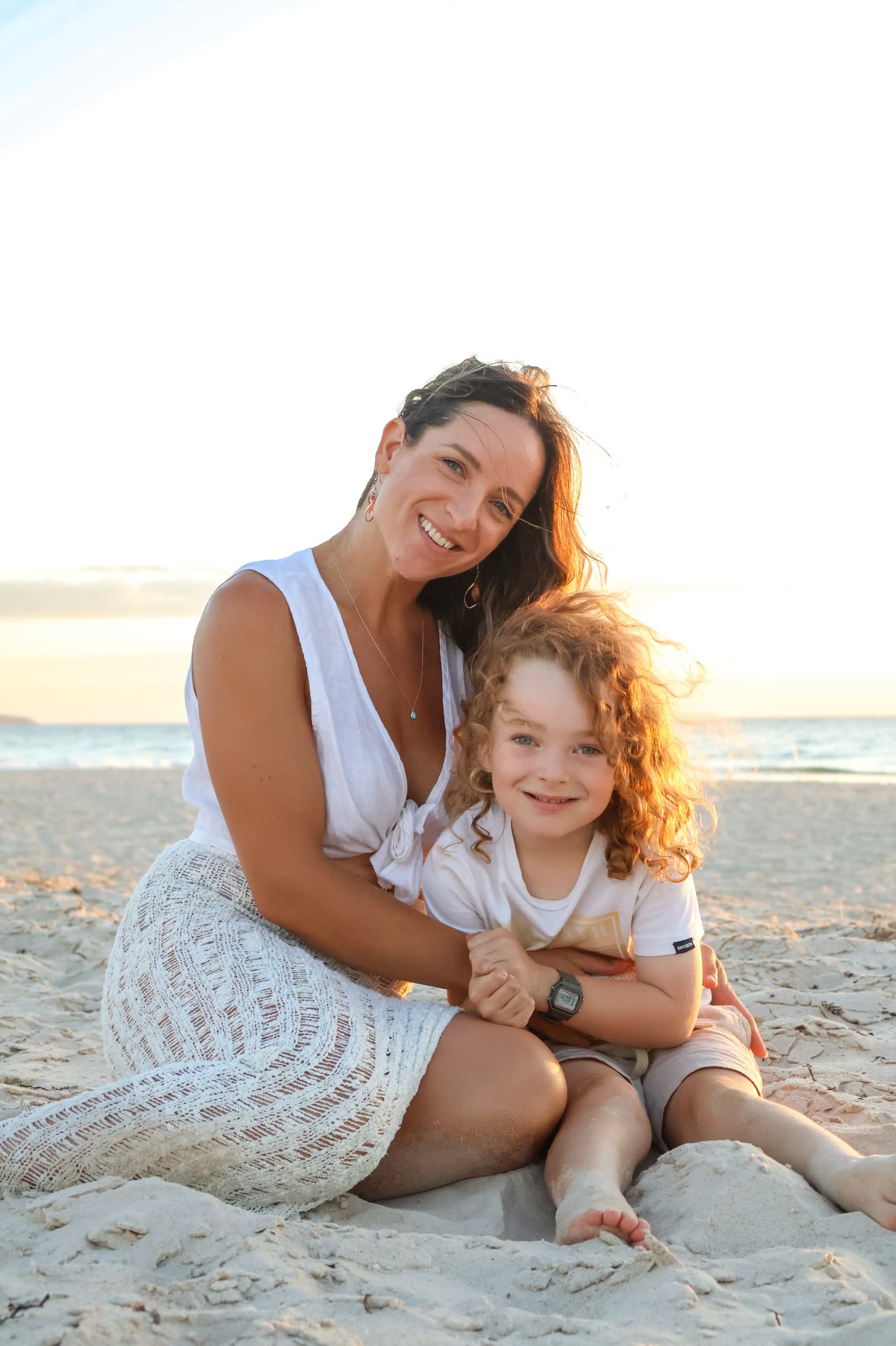 Mother and son laughing on the sand at sunset