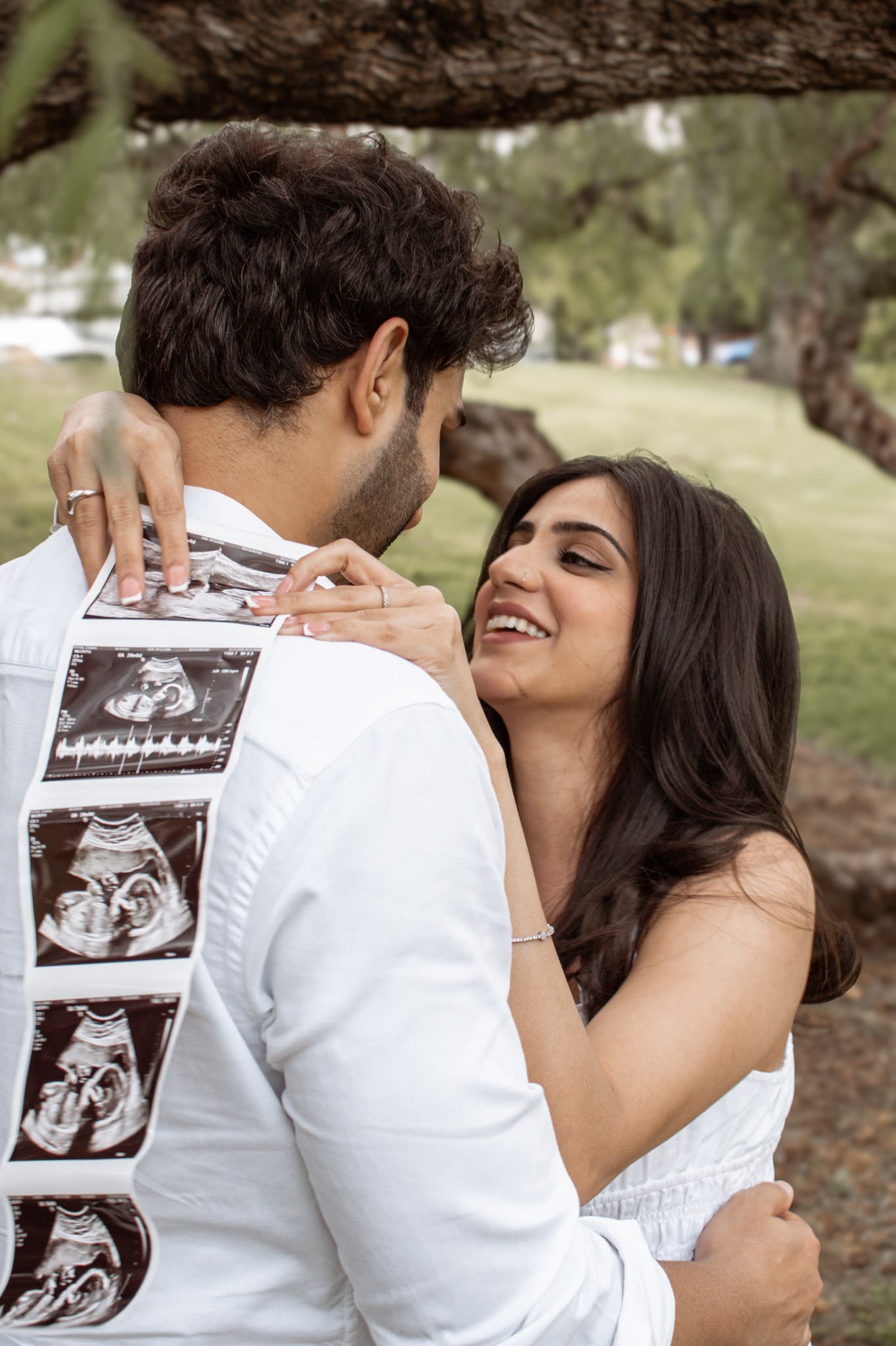 Couple sharing an ultrasound announcement under a tree
